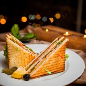 side-view-club-sandwich-with-salted-cucumbers-lemon-olives-round-white-plate (1)